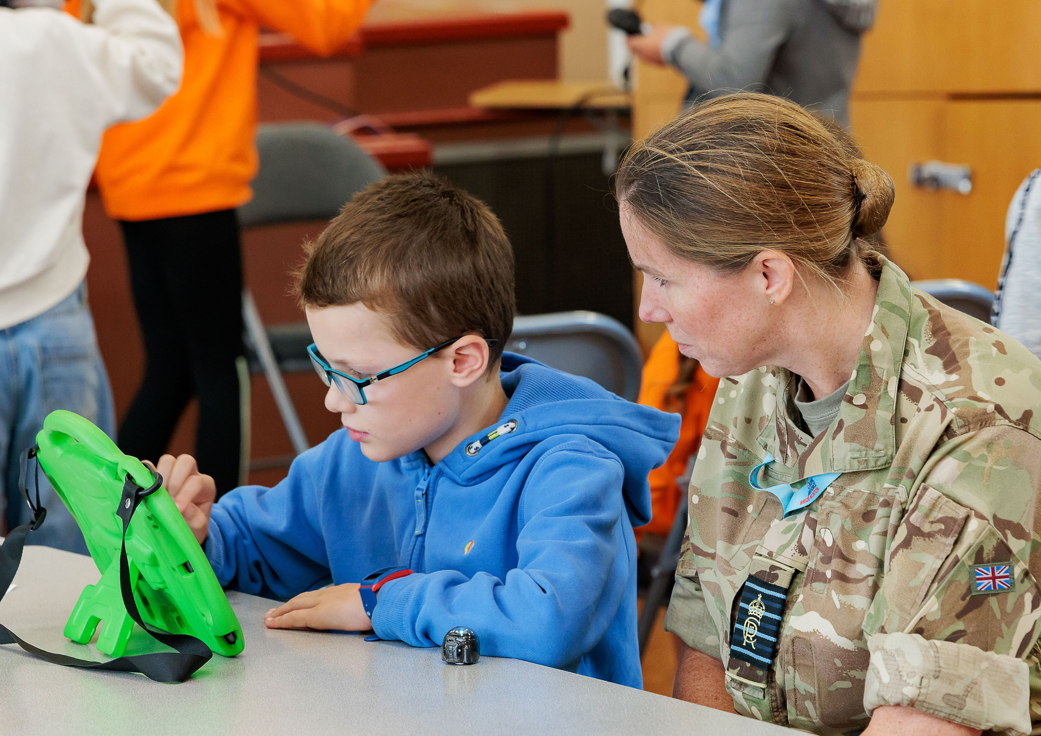 Photo: Royal Air Force Brize Norton Station Commander, Group Captain Louise Henton, sitting with a student, who is engaged in a STEM project on a tablet.
